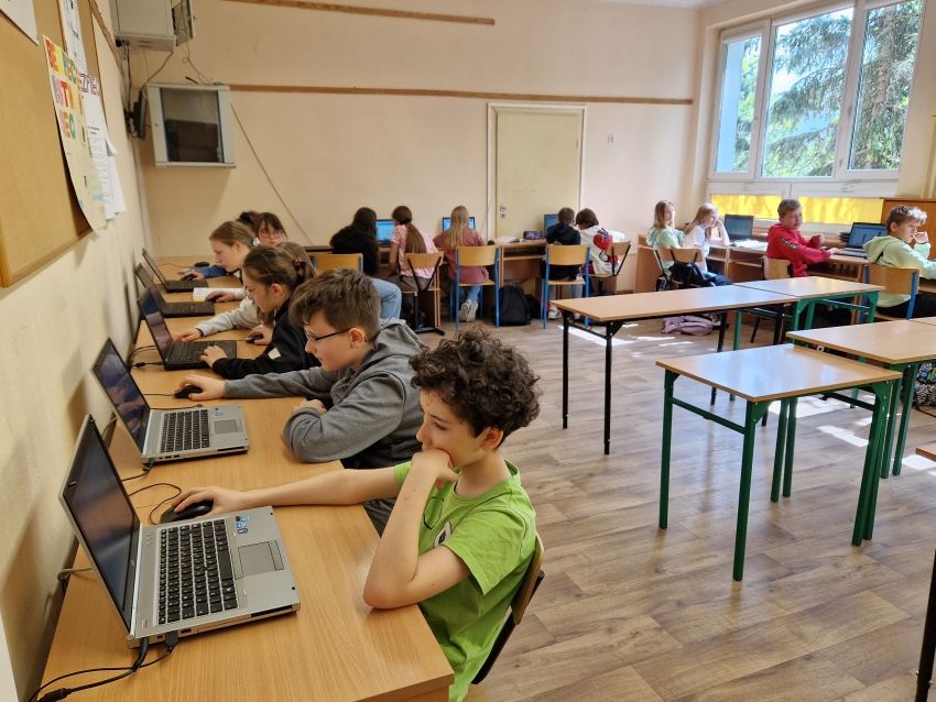 Dzieci w sali informatycznej siedzące przed laptopami